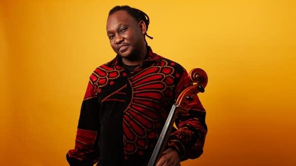 Poster A cellist stands before a yellow background with his instrument