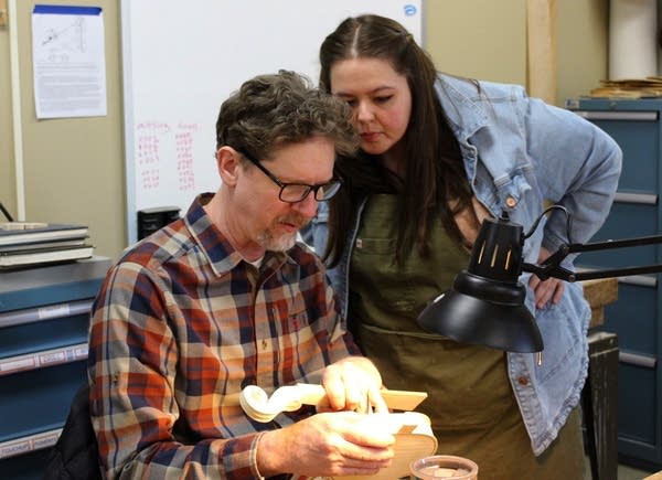 An instructor points to a student's violin project in progress and provides feedback