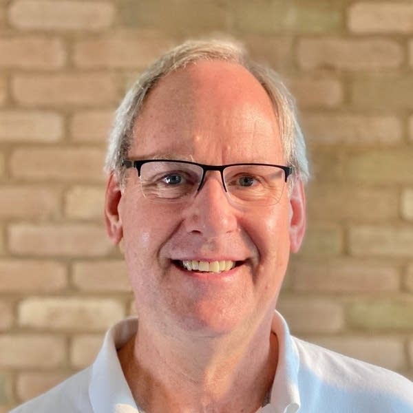 A man in glasses and a collared shirt smiles for a photo