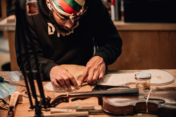 Poster A man places metal trim on a piece of wood that will become a violin